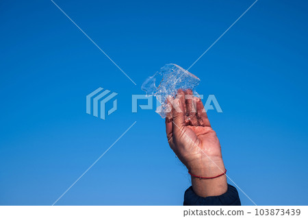 man's hand holds a piece of ice in winter against a blue sky 103873439