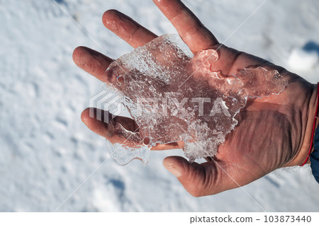 man's hand holds a piece of ice in winter 103873440