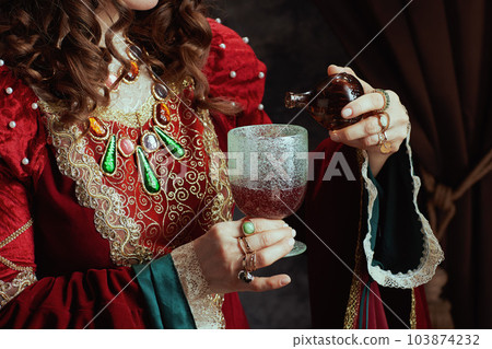 Medieval queen in red dress pouring poison into goblet Medieval queen in red dress pouring poison into goblet 103874232