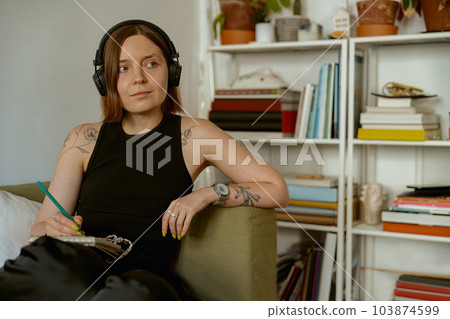 Female student listening to online lecture in headphones and making notes while studying from home Female student listening to online lecture in headphones and making notes while studying from home 103874599