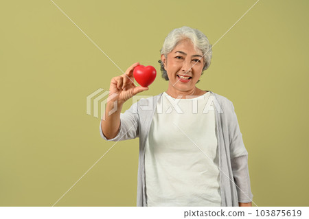 Beautiful senior woman holding a red heart and smiling to camera. Cardiology, medical and healthcare concept Beautiful senior woman holding a red heart and smiling to camera. Cardiology, medical and healthcare concept 103875619