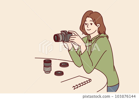 Woman photographer with camera sits at table choosing lens for photo essay or creating portrait 103876144