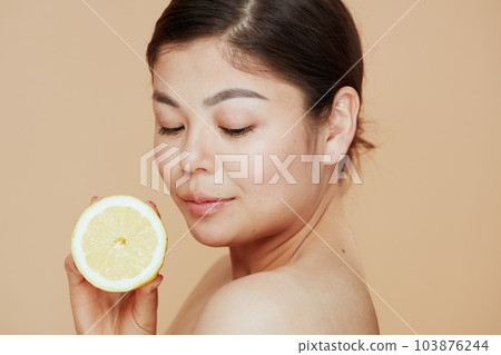 relaxed young asian woman with lemon on beige background 103876244