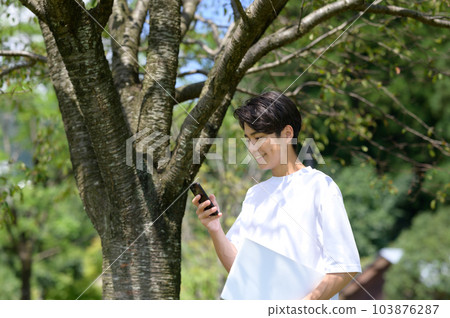 Young man holding smartphone and computer outdoors 103876287