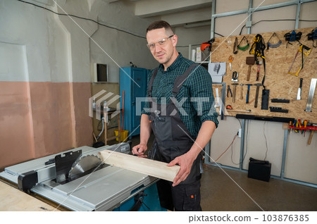 The carpenter cuts a wooden board on a circular machine. 103876385