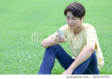 Young man sitting on grass and listening to music Young man sitting on grass and listening to music 103876750