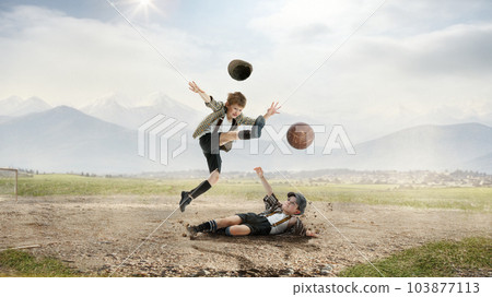 Little boys, children in retro style clothes playing football outdoors on a daytime, falling on dirt, kicking ball in jump 103877113