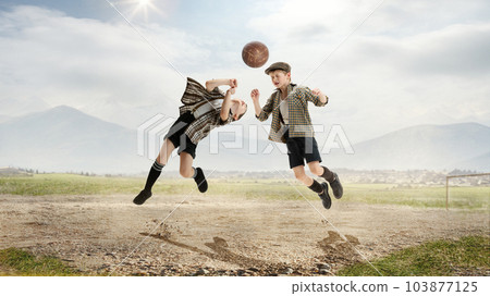 Head kick. Active little boys, children, friends in retro style clothes playing football outdoors on a daytime. Warm sunny day Head kick. Active little boys, children, friends in retro style clothes playing football outdoors on a daytime. Warm sunny day 103877125