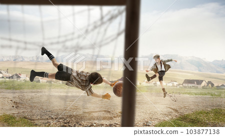 Two little boys, children in retro style clothes playing football outdoors on a daytime. Kicking ball into gate. Concentration Two little boys, children in retro style clothes playing football outdoors on a daytime. Kicking ball into gate. Concentration 103877138