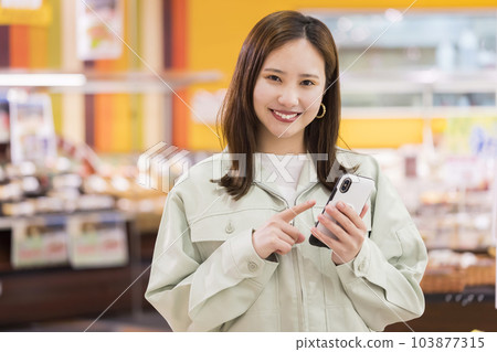 一位身穿工作服的年輕女性在超市操作智能手機 一位身穿工作服的年輕女性在超市操作智能手機 103877315