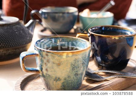 Brewing and Serving Tea. Teapot Poured Green Tea Blue Ceramic Cup on Wooden Cafe Table. Two Pottery Handmade Mugs Early in the Morning. Trendy Authentic Porcelain Set. Breakfast Concept. Tea Time 103878588