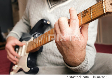 Senior man is playing guitar. Elderly man in a sweater learning to play. Enjoying retirement life. Senior man is playing guitar. Elderly man in a sweater learning to play. Enjoying retirement life. 103878589