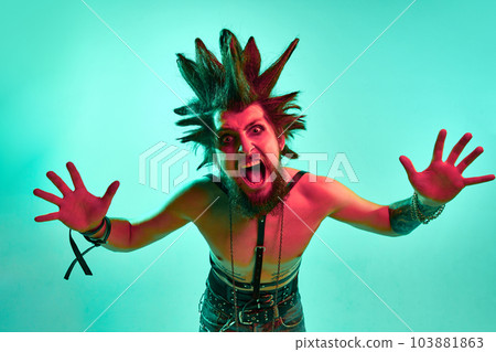 Portrait of young crazy looking man, punk with expressive hairstyle posing shirtless against blue studio background in neon light Portrait of young crazy looking man, punk with expressive hairstyle posing shirtless against blue studio background in neon light 103881863