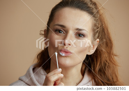 woman applying ointment using cotton swab against beige 103882501