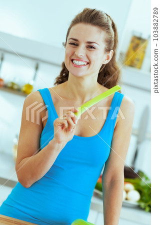 Smiling young woman eating celery in modern kitchen 103882789