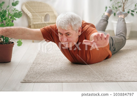 Happy smiling mature senior man doing exercises of gymnastics at home. Concept of healthy lifestyle, fitness, recreation, well being. Elderly male exercising training, stretching. Old man working out 103884797