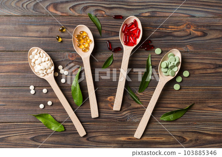 Top view Variety of vitamin and mineral pills in wooden spoon on Colored background. Top view of assorted pharmaceutical medicine pills. Dietary supplement healthcare product 103885346
