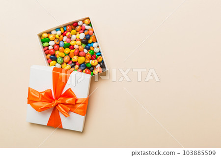 Set of different sweet candy in a paper box with a satin ribbon on a colored background. Holiday concept Set of different sweet candy in a paper box with a satin ribbon on a colored background. Holiday concept 103885509