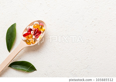 Vitamin capsules in a spoon on a colored background. Pills served as a healthy meal. Red soft gel vitamin supplement capsules on spoon 103885512