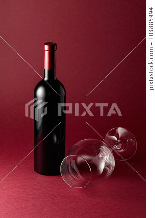 Bottle of red wine and an empty glass on a red background. 103885994
