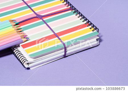Colored Pencils on stripy notepad notebook on lilac purple desk. Back to School stationery or drawing and creativity concept. Copy space 103886673