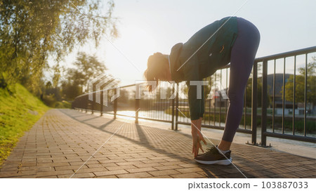 Sillhouette of attractive young woman stretching before her early morning run along the embankment of river. 103887033