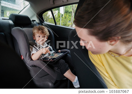 Cute little boy sitting in his car seat, playing on tablet. 103887067