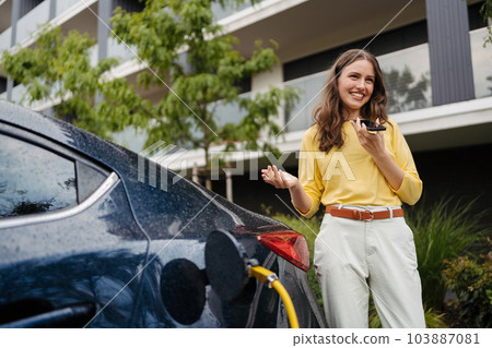Close up of beautiful woman calling using speakerphone while charging her electric car on the street. 103887081