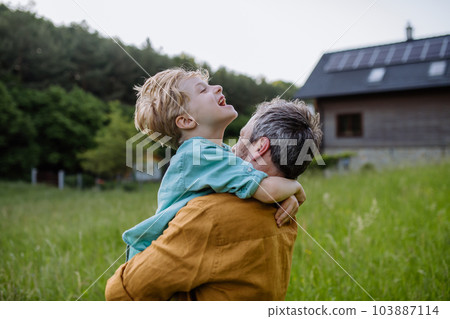 Rear view of father and his son looking at their house with solar panels on the roof. Rear view of father and his son looking at their house with solar panels on the roof. 103887114