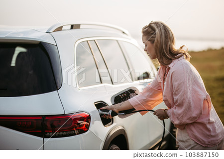 Woman charging her electric car, sustainable and economic transportation concept. Woman charging her electric car, sustainable and economic transportation concept. 103887150