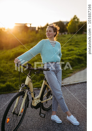 Young woman standing by electro bicycle, concept of commuting and ecologic traveling. Young woman standing by electro bicycle, concept of commuting and ecologic traveling. 103887166