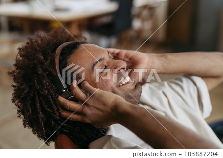 Portrait of young multiracial man listening music in office. 103887204