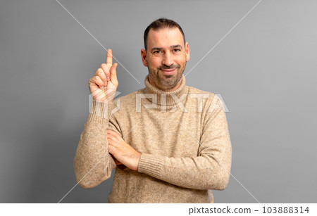 Insightful intelligent proactive man hispanic man in his 40s wearing a turtleneck sweater holding index finger up with a great new idea isolated on gray background studio portrait. People concept 103888314