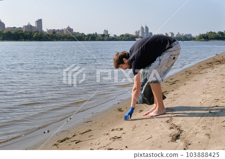 Man collecting plastic waste from a polluted beach using a garbage collector. 103888425