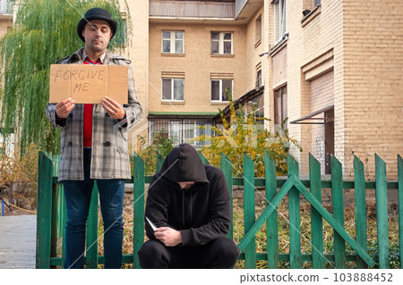 Forgiveness concept. Two men with a knife and a sign forgive me on a city street Forgiveness concept. Two men with a knife and a sign forgive me on a city street 103888452