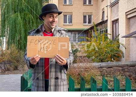 Cheerful man holding a sign with the text forgive me on the city street to ask for forgiveness 103888454