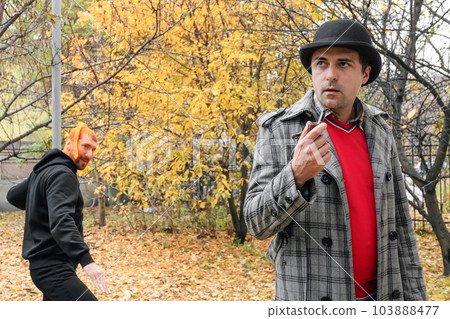A criminal in the park sneaks up to attack a man. Crime concept 103888477