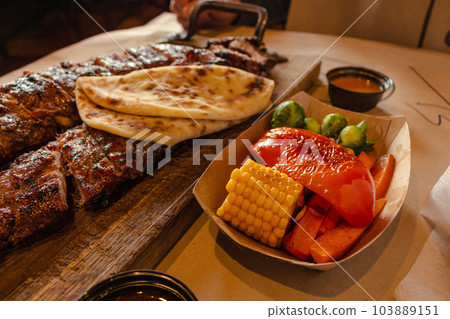 Grilled ribs with vegetables and bread. Smoked pork on wooden board and grilled vegetables. Dinner menu in restaurant. Medium roasted steak with corn, pepper and sauce. Pork ribs with ketchup. Grilled ribs with vegetables and bread. Smoked pork on wooden board and grilled vegetables. Dinner menu in restaurant. Medium roasted steak with corn, pepper and sauce. Pork ribs with ketchup. 103889151