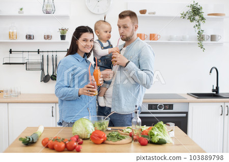 Kid giving daddy to drink juice while mom smiling at camera Kid giving daddy to drink juice while mom smiling at camera 103889798