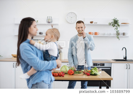Handsome dad cooking healthy meal while mother holding baby 103889799