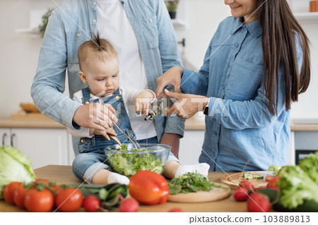 Mom dressing salad with oil while dad and kid mixing greens 103889813
