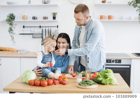 Family man and wife feeding daughter with red vegetable 103889909