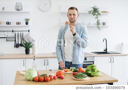 Man cutting vegetables with knife at dining table in kitchen 103890079