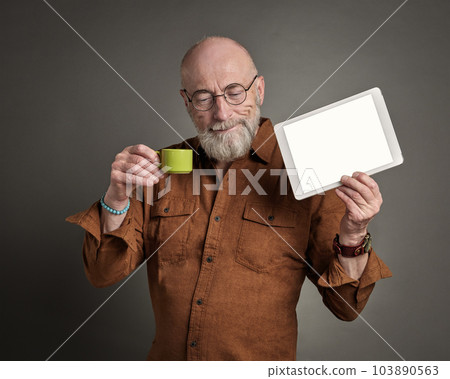 smiling senior man is drinking coffee and showing a blank digital tablet smiling senior man is drinking coffee and showing a blank digital tablet 103890563
