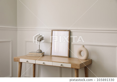 Modern living room, home office. Trendy round vase, beige lamp and old books. Blank picture frame mockup. Bamboo table with white drawers. Minimal Scandi boho interior, home. Beige wall background. Modern living room, home office. Trendy round vase, beige lamp and old books. Blank picture frame mockup. Bamboo table with white drawers. Minimal Scandi boho interior, home. Beige wall background. 103891330