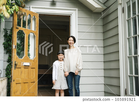 Portrait of a mother and daughter standing at the front door of their home 103891921