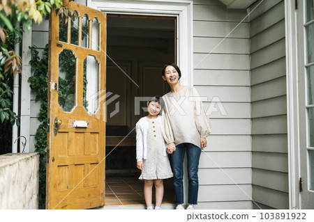 Portrait of a mother and daughter standing at the front door of their home 103891922