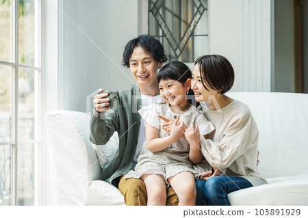 A family looking at a smartphone in the living room at home A family looking at a smartphone in the living room at home 103891929