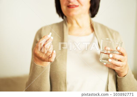 Retired woman in casual clothes at home holding pill and glass water.  103892771