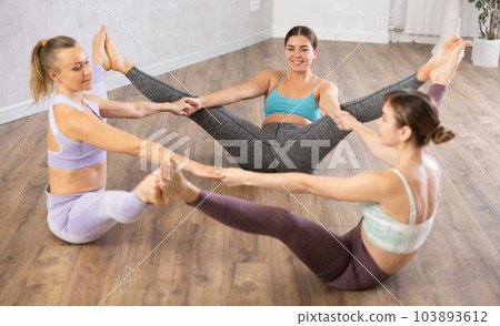 Three young women practicing yoga poses perform a joint exercise Three young women practicing yoga poses perform a joint exercise 103893612